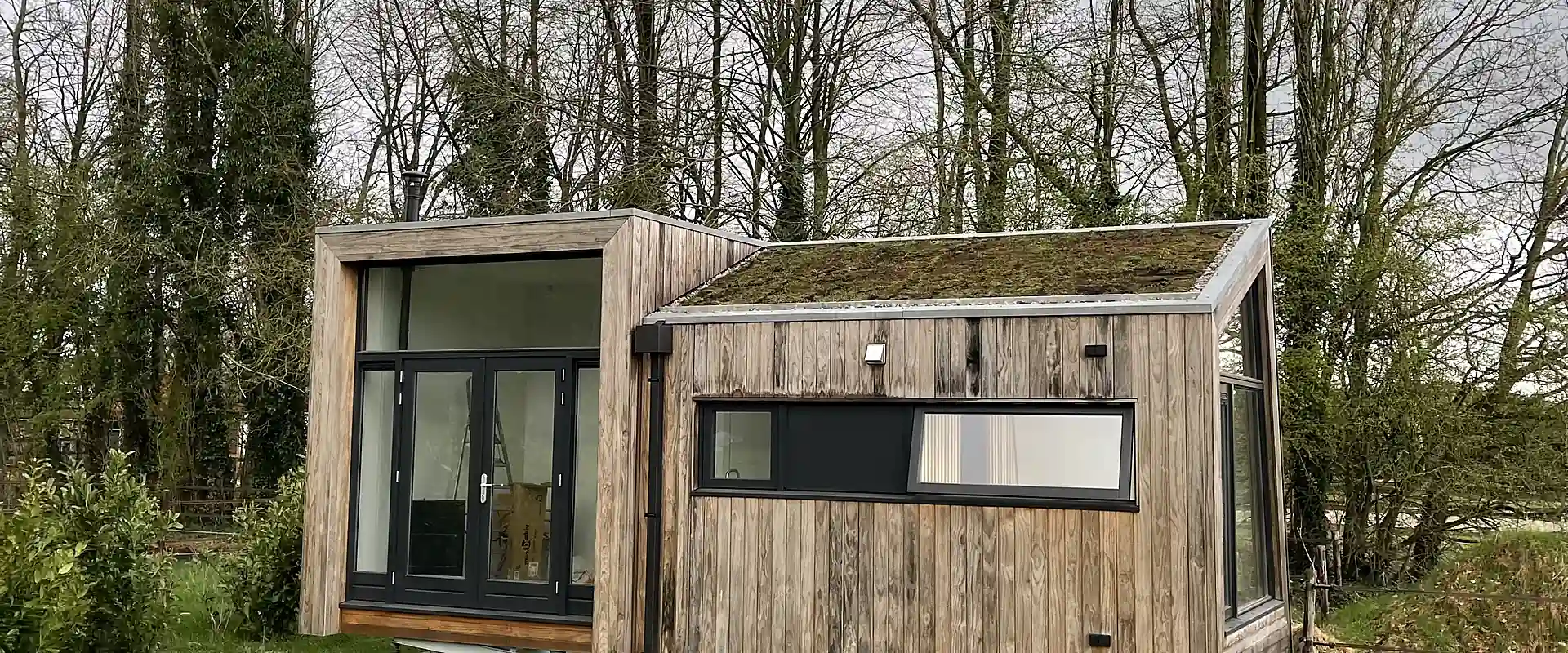Houten bijgebouw met een volgroeid sedumdak tussen de bomen