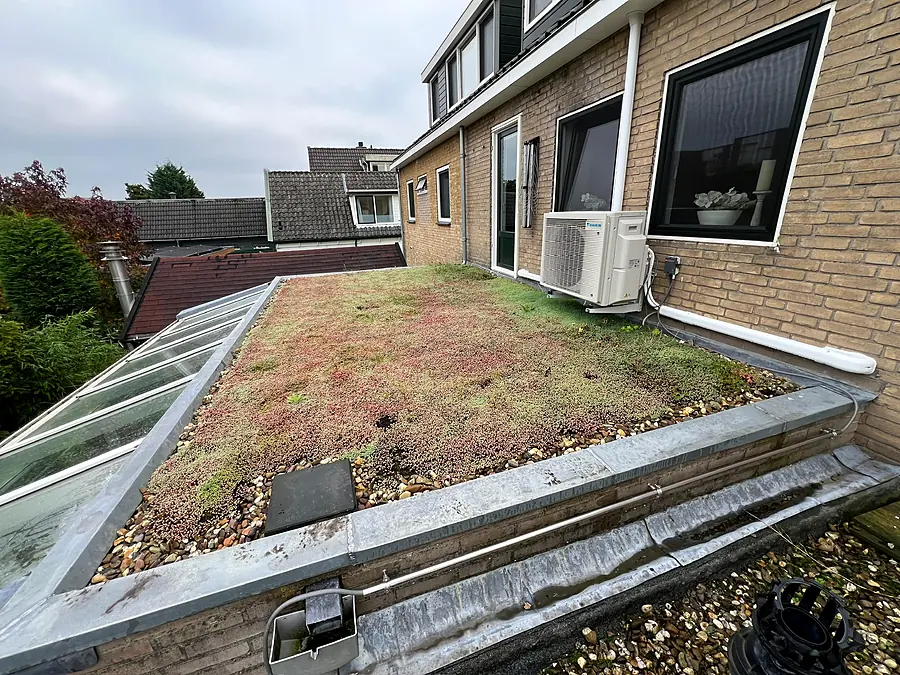 Plat sedumdak op een aanbouw naast een glazen serre, met buitenunit van de airco