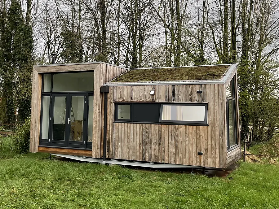 Houten bijgebouw met volgroeid sedumdak tussen de bomen
